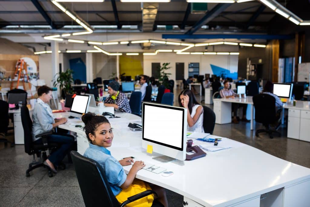 Balanced modern office scene symbolizing 'the right desk sharing ratio' with a mix of occupied and available desks, diverse employees, and a layout that exemplifies efficient and harmonious desk sharing.